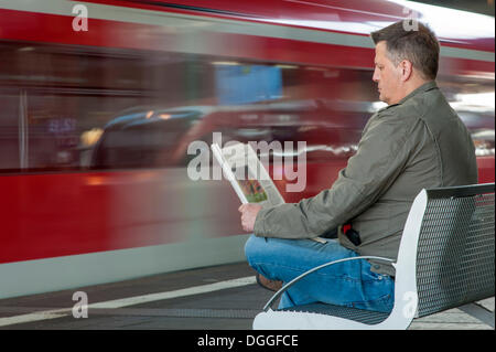 Homme assis sur un banc à la gare lire un journal, Düsseldorf, Rhénanie du Nord-Westphalie Banque D'Images