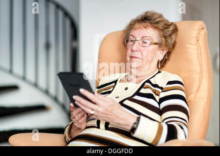 Femme âgée assise sur un fauteuil et de lire un eBook Banque D'Images