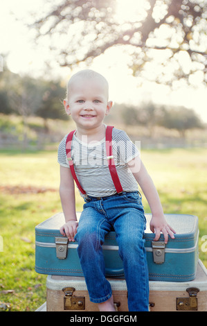 Jeune garçon assis sur des valises outdoors, portrait Banque D'Images