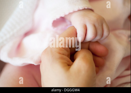 Baby Girl holding Mid adult woman's finger, Close up Banque D'Images