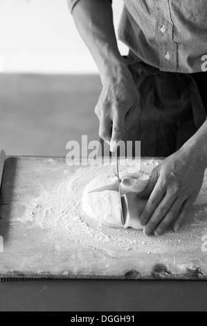 Young baker slicing pâte fraîche Banque D'Images