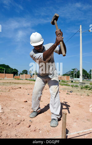 Homme avec un marteau de frapper un clou dans le sol, les gens des bidonvilles, favelas, travaillant ensemble sur un chantier de construction de la Banque D'Images