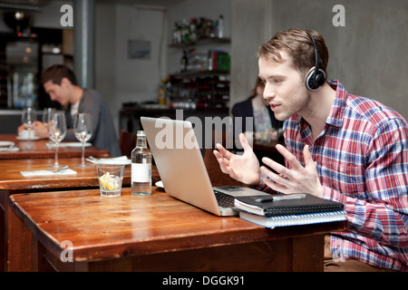 Young man wearing headphones using laptop in cafe Banque D'Images