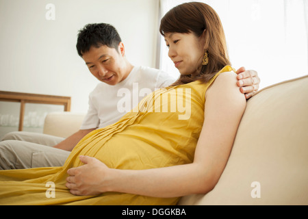 L'homme à la recherche de la femme enceinte à l'estomac sur canapé Banque D'Images