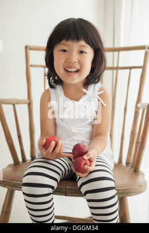 Girl sitting on wooden chair holding apples, portrait Banque D'Images