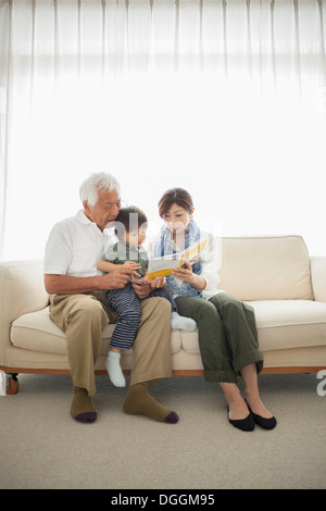Lecture de la mère en fils assis sur les genoux de grand-père Banque D'Images