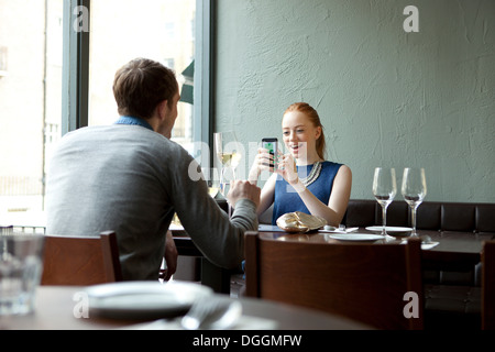 Young couple in restaurant, woman using cell phone Banque D'Images