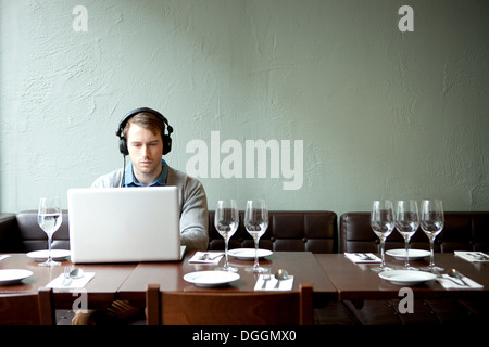 Young man wearing headphones using laptop in restaurant Banque D'Images