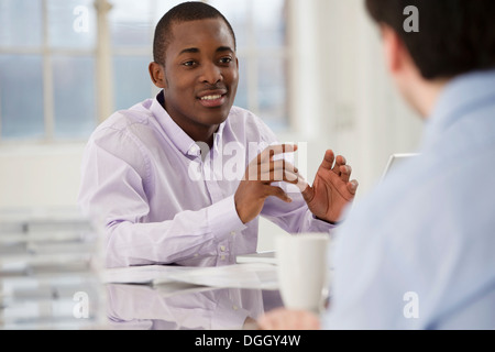 Hommes d'sitting at desk talking Banque D'Images