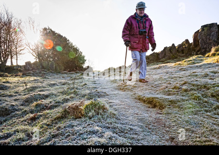 Homme âgé marcher avec un bâton de marche sur l'herbe couverte de givre avec des rochers escarpés dans l'arrière-plan. Banque D'Images