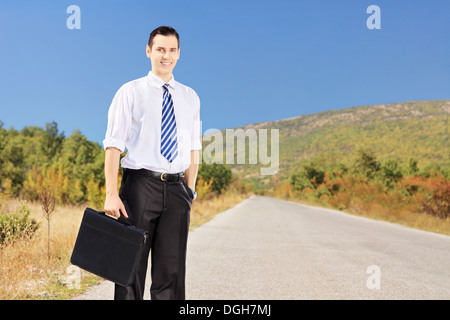 Jeune homme tenant une valise confiant sur une route Banque D'Images