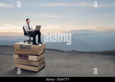 Employée de bureau assis sur une pile de livres géants dans un désert à l'aide d'un ordinateur portable Banque D'Images