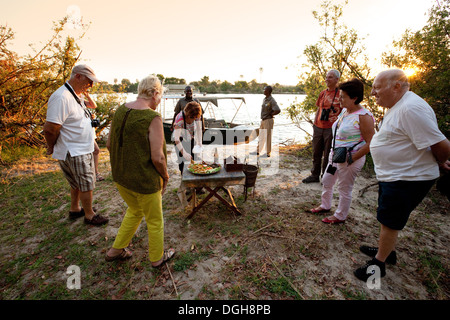 Les touristes de prendre une pause alimentaire sur une rivière Zambezi safari croisière au coucher du soleil, la Zambie, l'Afrique Banque D'Images