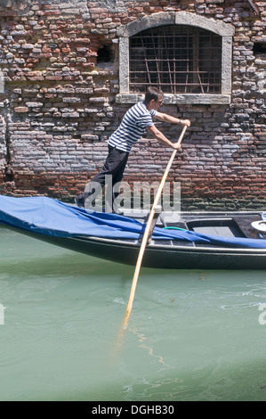 Un jeune homme gondolier pousse sur sa rame pour propulser sa cabine dans un canal de Venise, Italie, Europe Banque D'Images