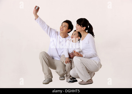 La famille de l'Asie de l'est avec un enfant, enlacés, accroupi sur le sol, l'appareil photo avec téléphone mobile Banque D'Images