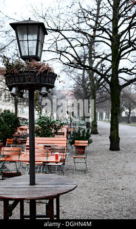 Une lampe et les tables et les chaises vides en hiver, Cour Jardin, Munich, Bavière Banque D'Images