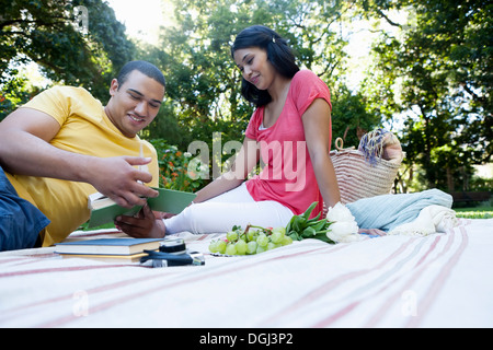 Young couple sitting on picnic blanket, Man reading book Banque D'Images