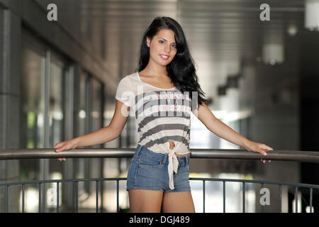 Jeune femme dans un T-shirt à rayures et denim short, qui posent avec une balustrade Banque D'Images