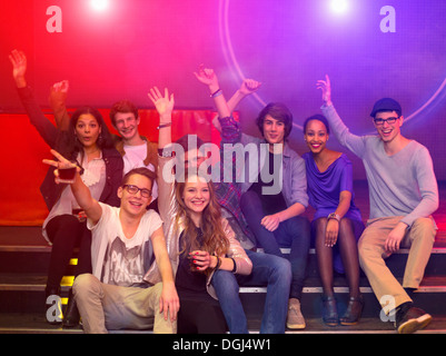 Groupe d'adolescents et jeunes adultes à partie holding drinks et raising arms Banque D'Images