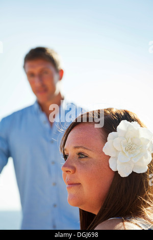 Jeune femme avec une fleur dans ses cheveux dans le profil à l'écart des hommes debout derrière, n'est pas mise au point, à la recherche d'elle, outdors, Banque D'Images