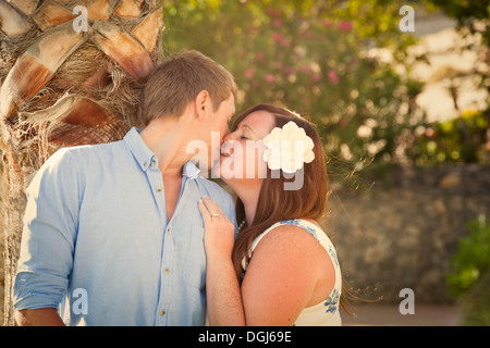 Couple espiègle et taquine en sous jardin tropical avec des palmiers et de fleurs, à la fin de soir chaud, lumière douce. Banque D'Images