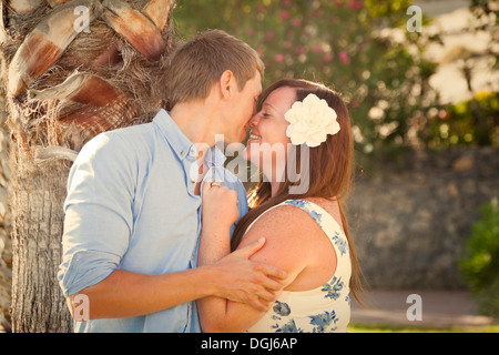 Couple espiègle et taquine en sous jardin tropical avec des palmiers et de fleurs, à la fin de soir chaud, lumière douce. Banque D'Images