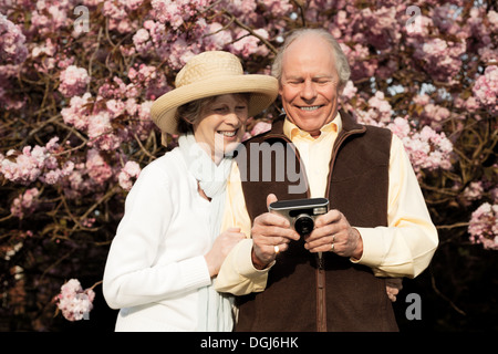 Mari et femme de sourire et à la recherche à l'appareil photo en main Banque D'Images