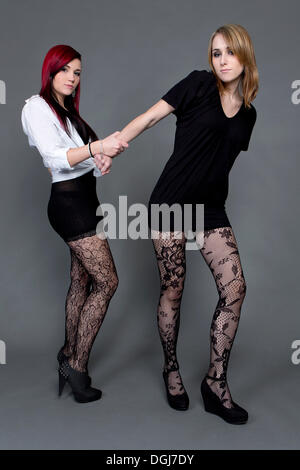 Deux jeunes femmes portant des jupes, collants et talons hauts se tenant Banque D'Images