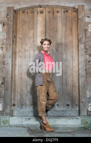 Jeune femme portant des pantalons en cuir traditionnel posant devant une porte en bois, dirndl rechercher Banque D'Images