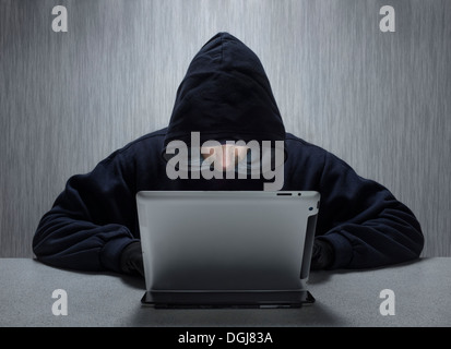 Un capuchon à l'aide d'un homme anonyme ordinateur tablette pour représenter un cyber criminel. Banque D'Images