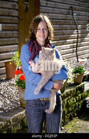 Jeune femme à l'extérieur d'une maison avec un chat gris dans ses bras. Banque D'Images