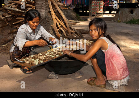 Femme khmère et une fille de sucre de palme caramélisé de remplissage dans des petits moules constitué de bandes de feuilles de palmier pour la production de Banque D'Images