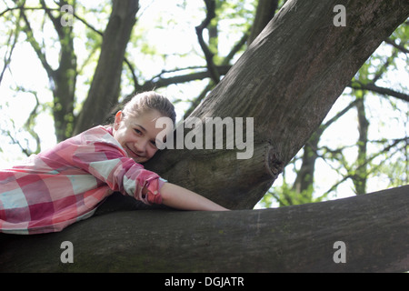 Portrait of young girl lying on top of tree branch Banque D'Images