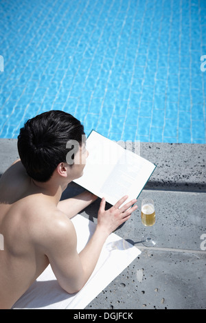 Un homme lisait un livre près de la piscine Banque D'Images