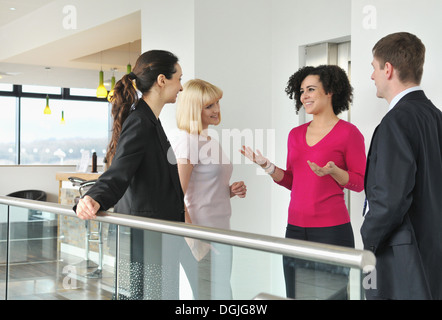 Quatre collègues parler by railing in office building Banque D'Images