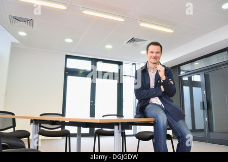 Male office worker sitting on table in office Banque D'Images