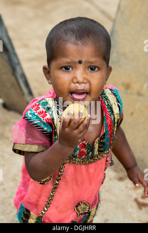 Basse caste indien baby girl eating a indian sweet / ladu. L'Andhra Pradesh, Inde Banque D'Images