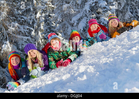 Six jeunes souriant allongé sur la pente de neige en face d'une forêt couverte de neige, Flachau, Salzbourg, Autriche, Europe Banque D'Images