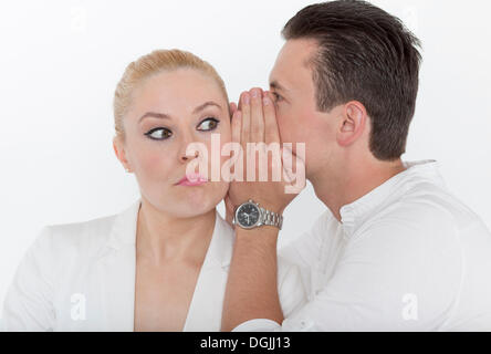 Jeune homme murmurer quelque chose à l'oreille de son jeune partenaire, qu'elle reçoit avec un regard sceptique, image symbolique pour Banque D'Images