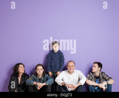 Garçon, debout au milieu de la famille assise en face de fond violet Banque D'Images