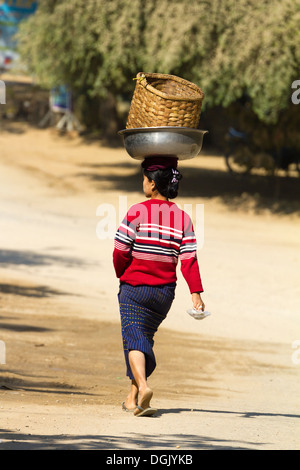 Une femme marche tout en équilibrant un panier sur sa tête à Bagan au Myanmar. Banque D'Images