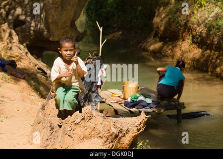 Un jeune garçon par un ruisseau alors que sa mère ne l'en laver Inn Thein Village. Banque D'Images