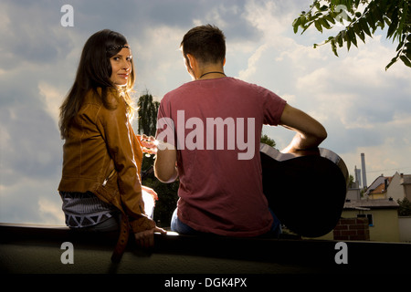 Couple sitting on wall, man playing guitar Banque D'Images