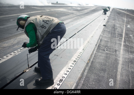 Maître de Manœuvre de l'aviation (Équipement) Airman Jeremy Lucas s'occupe de l'entretien d'une catapulte sur le pont de vol de l'aéronef Banque D'Images