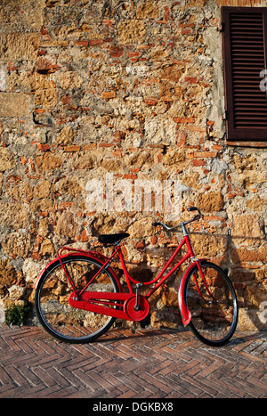 Vintage bicycle rouge garée contre mur en vieille ville. Banque D'Images