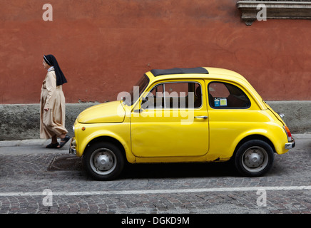 Une nonne passe un jaune vintage Fiat 500 à Bologne. Banque D'Images