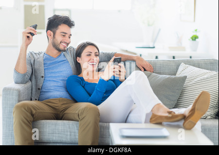 Couple relaxing on sofa with cell phones Banque D'Images