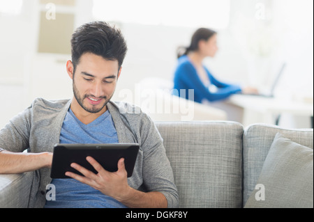 Man sitting on sofa using digital tablet, woman in background Banque D'Images