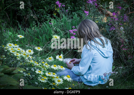 Une fille assise avec des fleurs dans un jardin. Banque D'Images