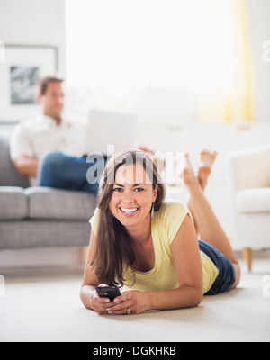 Femme couchée sur l'avant et à l'aide de téléphone mobile, man in background Banque D'Images